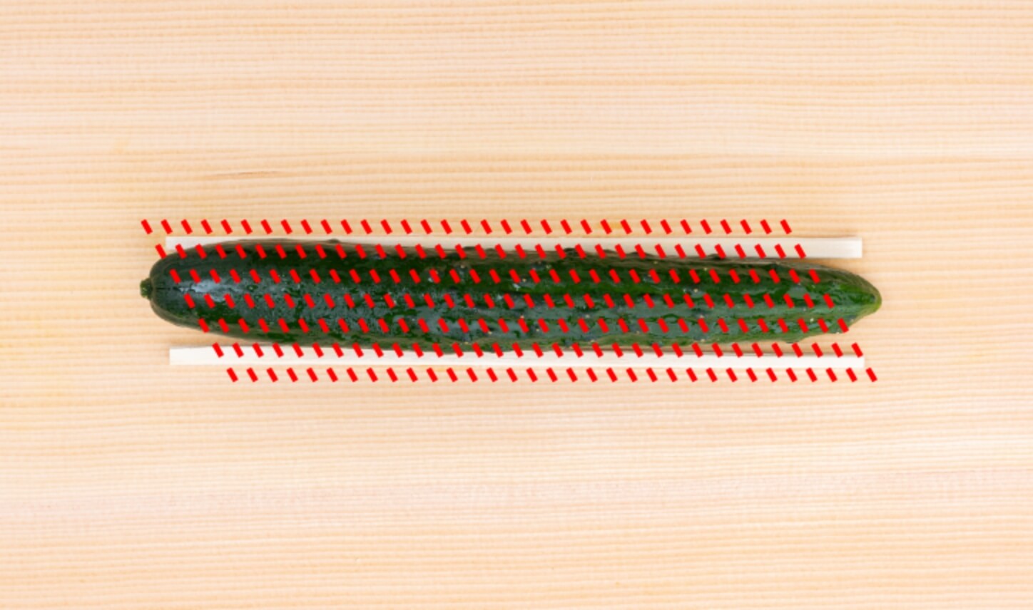 きゅうりを2本の割り箸で挟み、包丁が割り箸に当たるまで、1～2mmの間隔で斜めに切り込みを入れます。